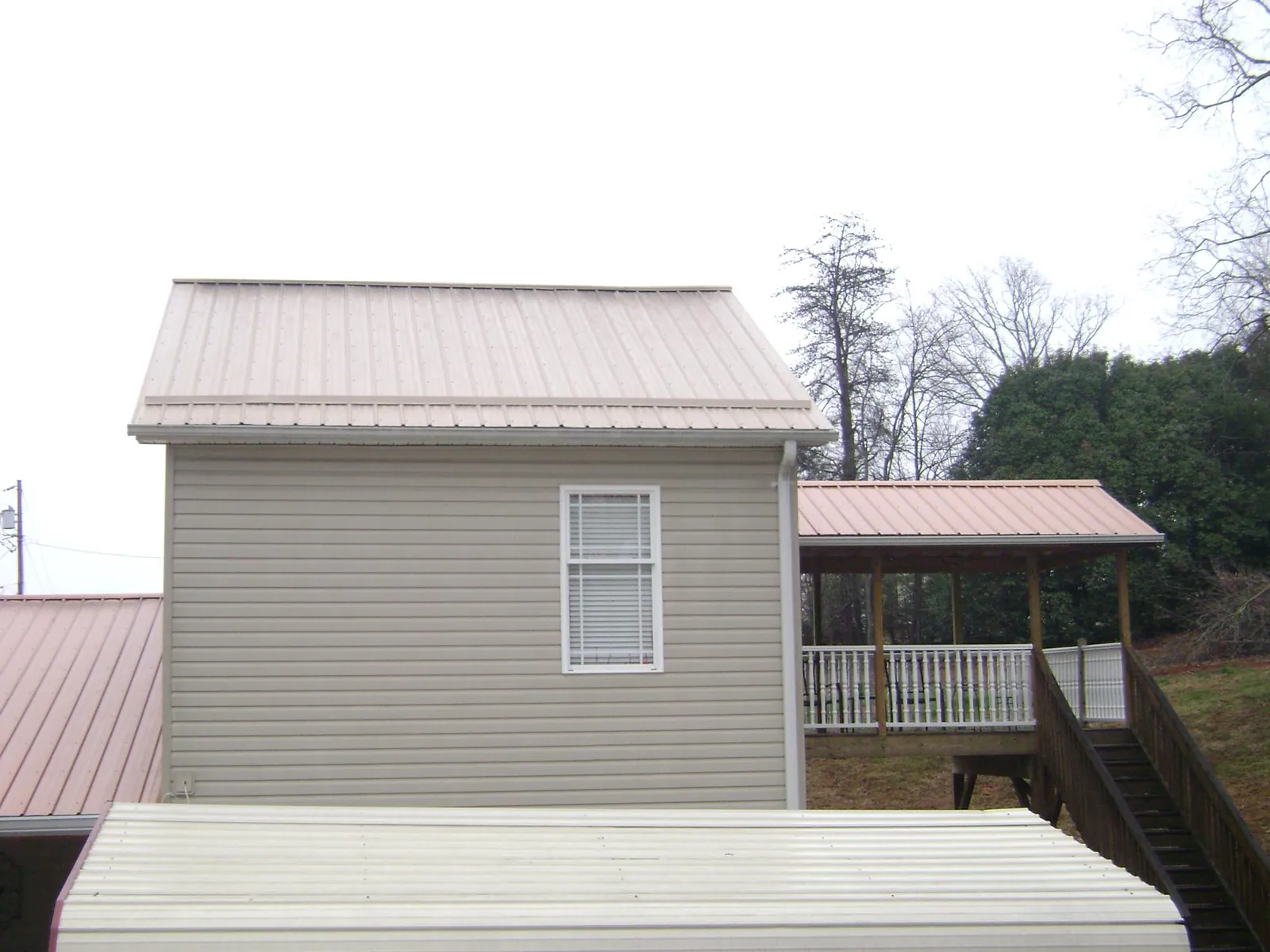 Tan metal roofs on a two story addition and attached porch, from a Roof Replacement job in Florence